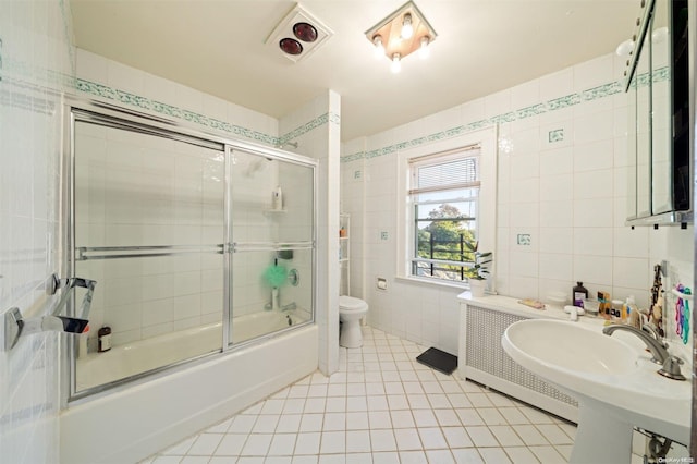 bathroom featuring tile patterned flooring, bath / shower combo with glass door, tile walls, and toilet