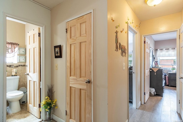 hallway featuring light wood-type flooring and tile walls