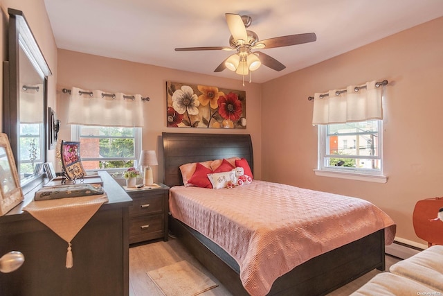 bedroom featuring ceiling fan, a baseboard heating unit, light hardwood / wood-style flooring, and multiple windows