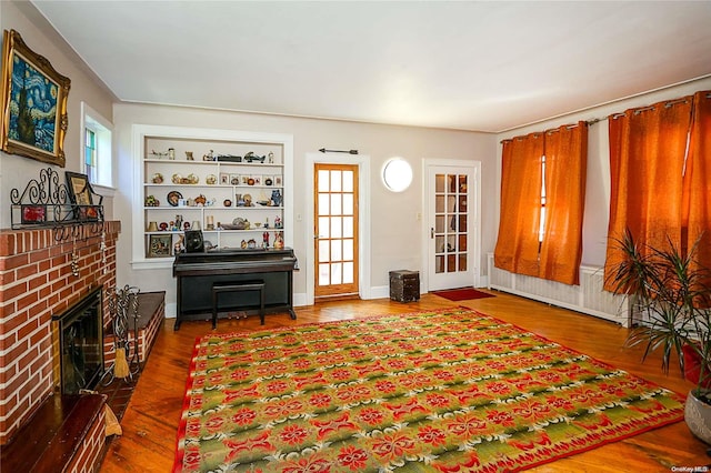 sitting room with built in features, wood-type flooring, a fireplace, and a wealth of natural light