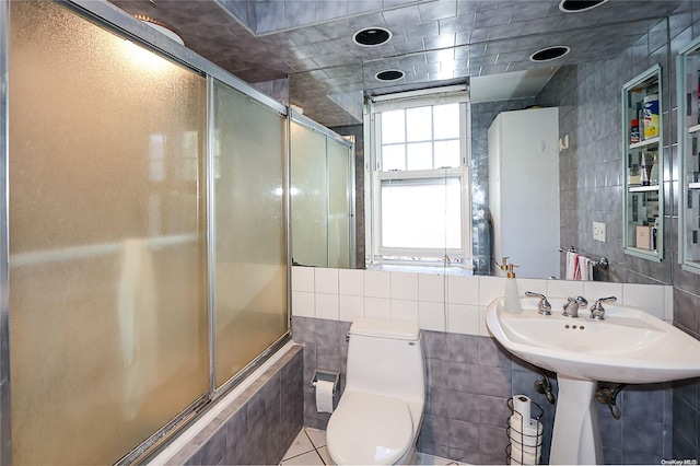 bathroom with tile patterned flooring, combined bath / shower with glass door, tile walls, and toilet