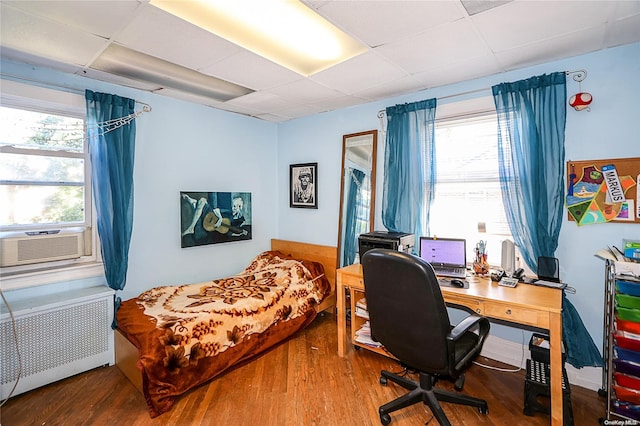 bedroom featuring hardwood / wood-style flooring, a paneled ceiling, cooling unit, and radiator heating unit