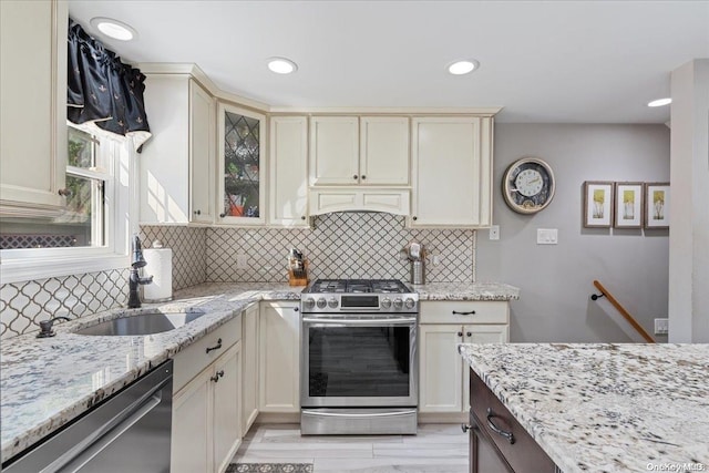 kitchen with light stone countertops, sink, stainless steel appliances, cream cabinetry, and decorative backsplash