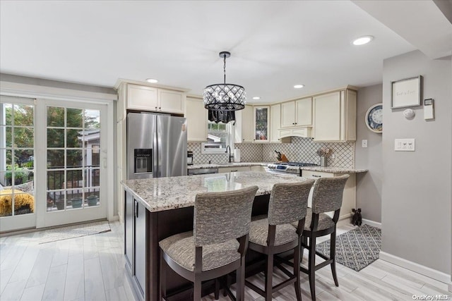 kitchen featuring light stone countertops, sink, hanging light fixtures, light hardwood / wood-style flooring, and appliances with stainless steel finishes