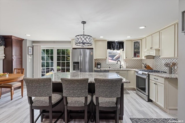 kitchen featuring pendant lighting, a kitchen island, appliances with stainless steel finishes, cream cabinetry, and light hardwood / wood-style floors