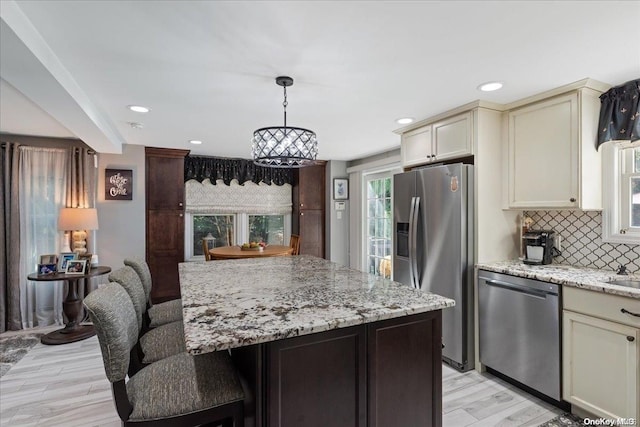 kitchen with cream cabinets, hanging light fixtures, light wood-type flooring, tasteful backsplash, and stainless steel appliances