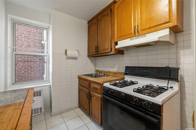 kitchen featuring radiator, gas range gas stove, sink, light tile patterned flooring, and tile walls