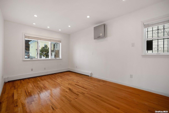 spare room with a baseboard heating unit, a wall unit AC, and light hardwood / wood-style flooring