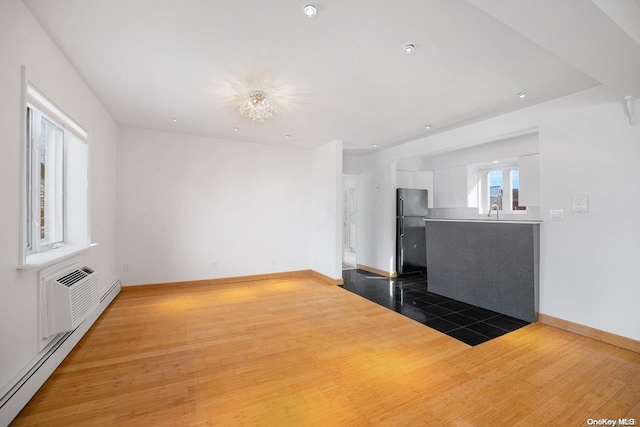 unfurnished living room with a healthy amount of sunlight, dark hardwood / wood-style flooring, sink, and a baseboard radiator