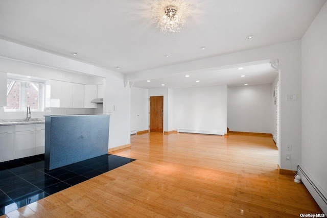 unfurnished living room featuring hardwood / wood-style floors, sink, and a baseboard heating unit