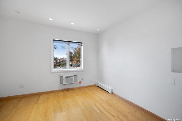 spare room featuring light wood-type flooring, a wall unit AC, and a baseboard radiator