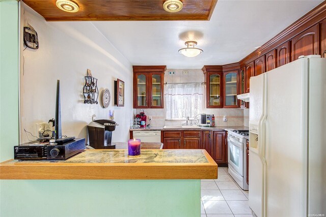 kitchen with tasteful backsplash, kitchen peninsula, sink, and white appliances