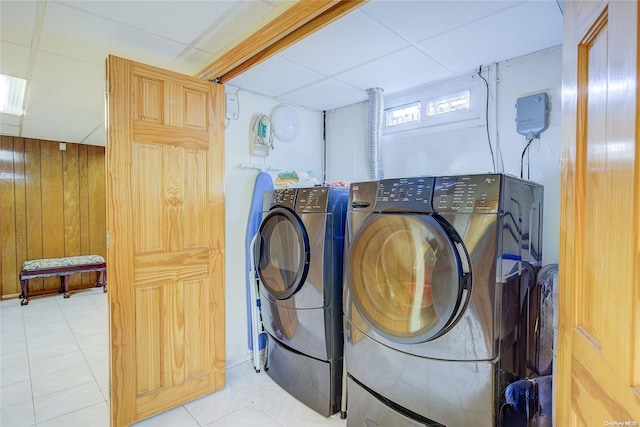 clothes washing area with light tile patterned floors, separate washer and dryer, and wood walls