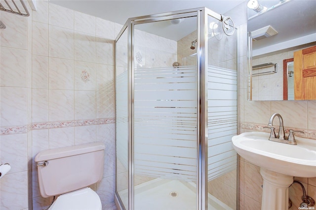 bathroom featuring a shower with door, tile walls, and toilet