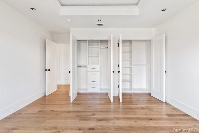 unfurnished bedroom featuring a tray ceiling, baseboards, light wood finished floors, and two closets