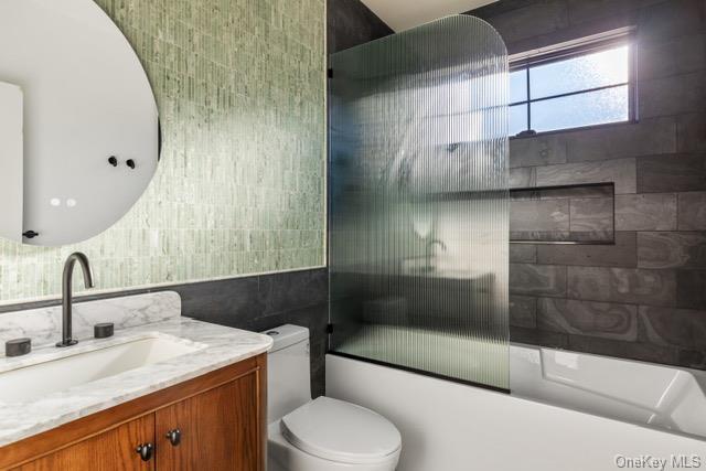 bathroom with toilet, bath / shower combo with glass door, vanity, and tile walls