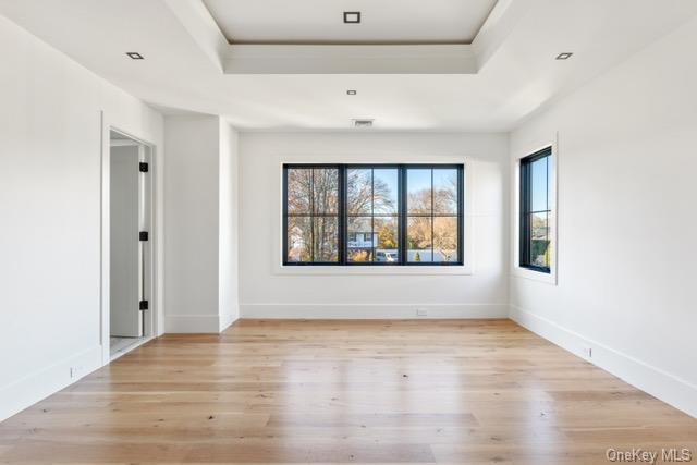 spare room with a tray ceiling, wood finished floors, and baseboards