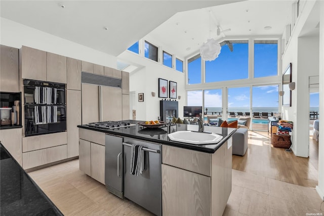 kitchen with sink, a high ceiling, light hardwood / wood-style flooring, black double oven, and an island with sink