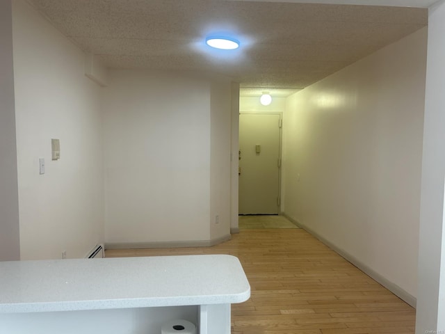 corridor with light hardwood / wood-style flooring and a baseboard heating unit