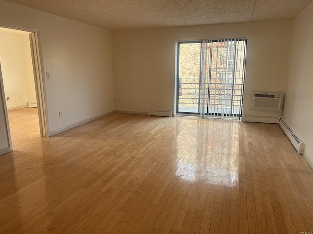 empty room featuring light hardwood / wood-style floors, a wall mounted AC, and a baseboard heating unit