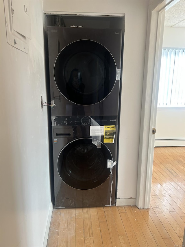 washroom with stacked washer and dryer, a baseboard radiator, and light hardwood / wood-style flooring