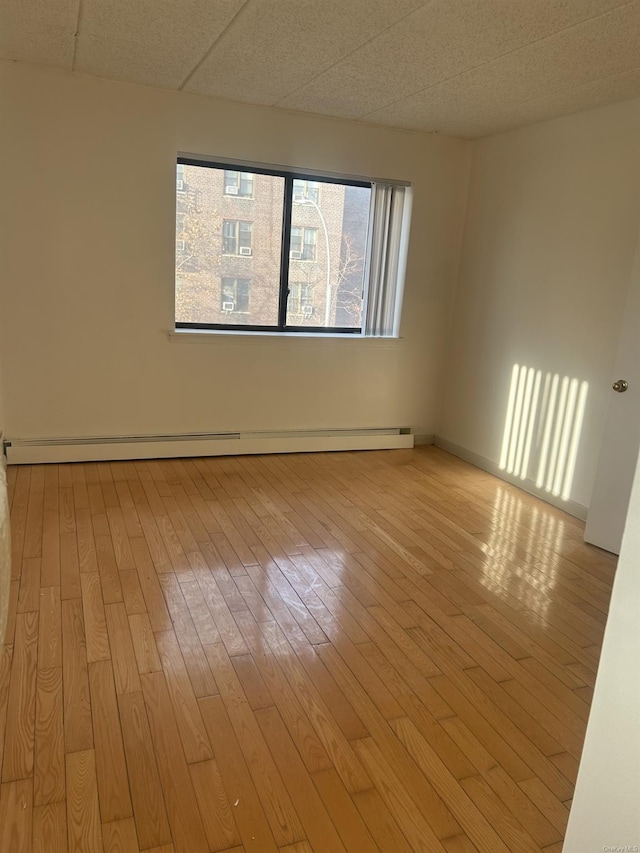 empty room with a paneled ceiling, light wood-type flooring, and a baseboard radiator