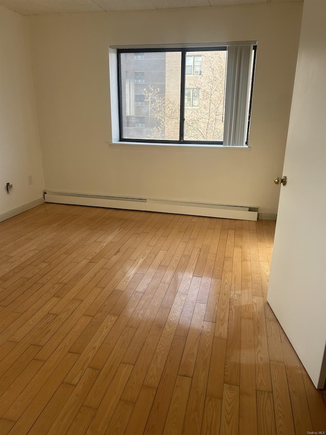 empty room featuring a baseboard heating unit and light wood-type flooring