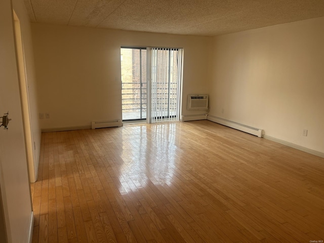 empty room with baseboard heating, light hardwood / wood-style floors, and an AC wall unit