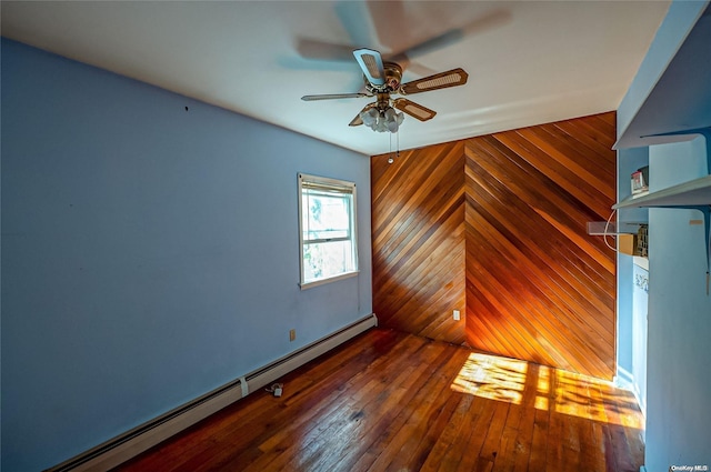 spare room with ceiling fan, baseboard heating, wooden walls, and dark wood-type flooring