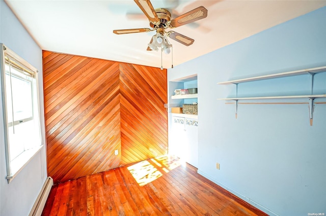 empty room featuring wood walls, ceiling fan, a baseboard heating unit, and hardwood / wood-style flooring