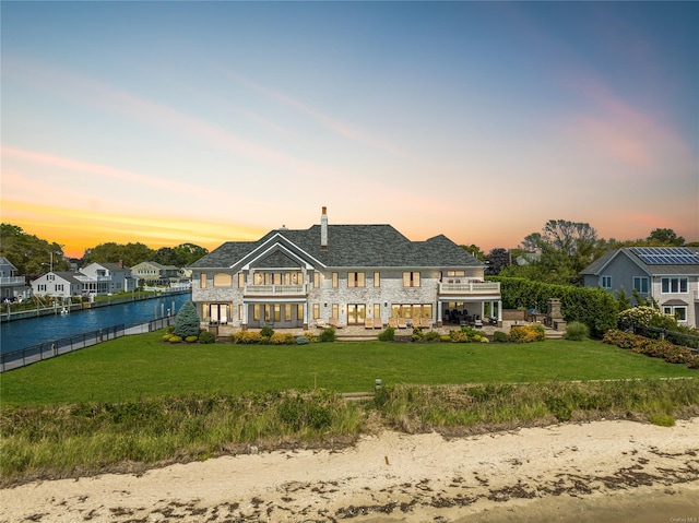 back house at dusk featuring a yard, a balcony, and a water view