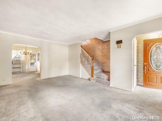 unfurnished living room featuring carpet, crown molding, and an inviting chandelier