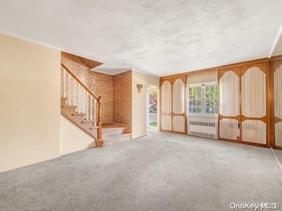 unfurnished living room with carpet, radiator heating unit, and crown molding