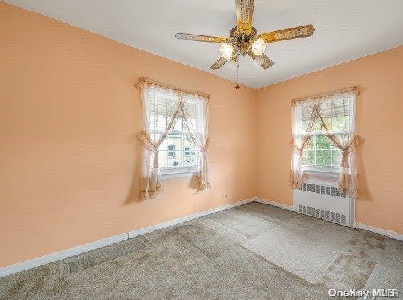 empty room with light carpet, radiator heating unit, and plenty of natural light