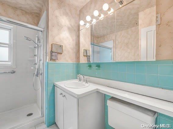 bathroom with vanity, toilet, an enclosed shower, and tile walls