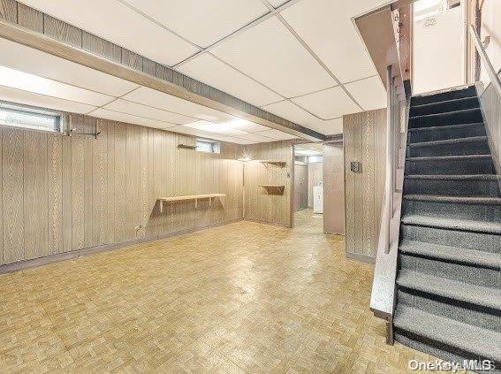 basement featuring a paneled ceiling, light parquet floors, and wooden walls