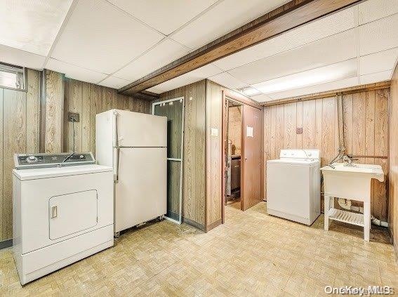 clothes washing area featuring sink, washing machine and dryer, wooden walls, and light parquet flooring