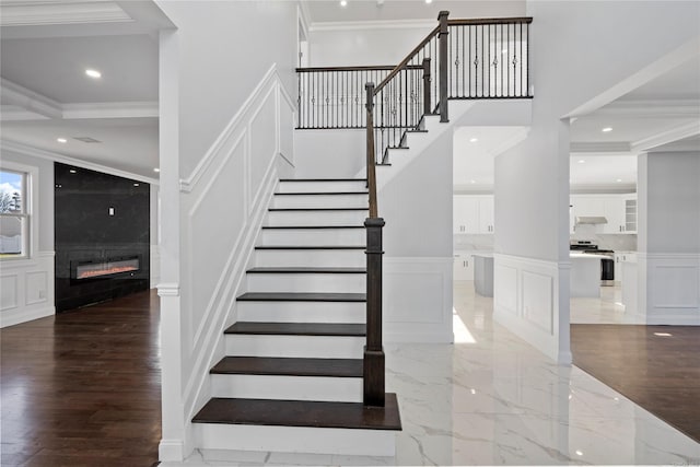 stairway featuring wood-type flooring, ornamental molding, and a fireplace