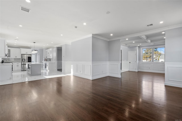 unfurnished living room featuring ornamental molding, beam ceiling, dark wood-type flooring, and sink