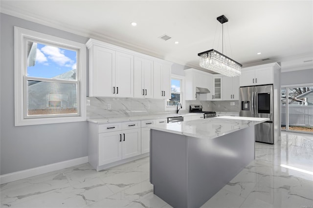 kitchen featuring backsplash, appliances with stainless steel finishes, decorative light fixtures, a kitchen island, and white cabinetry