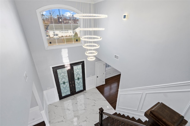 foyer with hardwood / wood-style floors, a chandelier, a high ceiling, and french doors