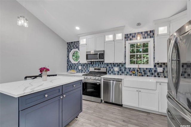 kitchen with appliances with stainless steel finishes, backsplash, vaulted ceiling, white cabinetry, and hanging light fixtures