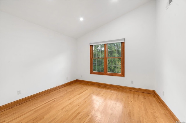 spare room with light wood-type flooring and lofted ceiling