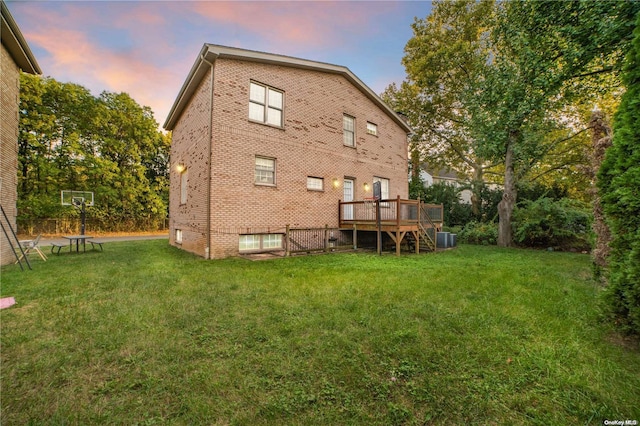 back house at dusk with a yard, central AC, and a wooden deck