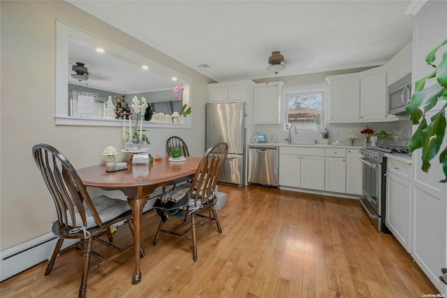 kitchen featuring stainless steel appliances, baseboard heating, sink, light hardwood / wood-style flooring, and white cabinets