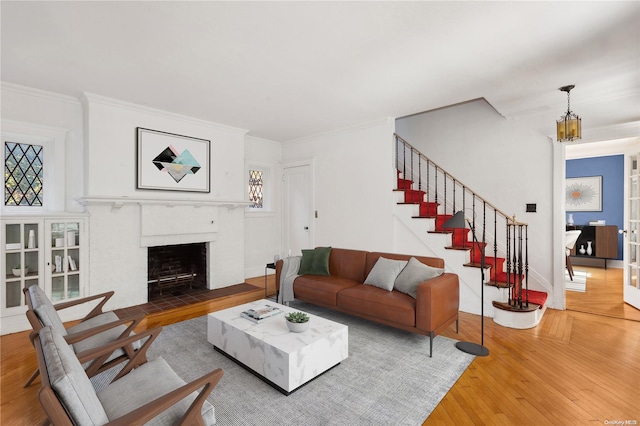 living room with french doors, a brick fireplace, crown molding, wood-type flooring, and an inviting chandelier