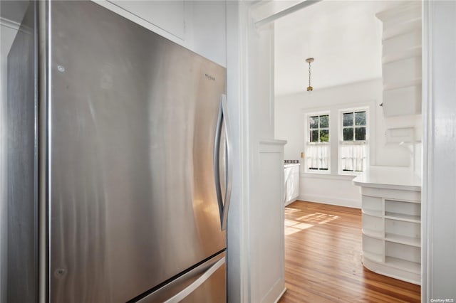 kitchen featuring light wood-type flooring, hanging light fixtures, and stainless steel refrigerator