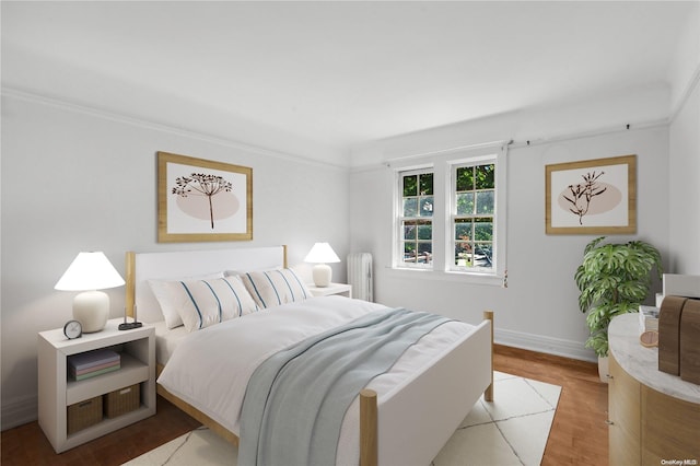 bedroom with radiator heating unit, crown molding, and light hardwood / wood-style flooring