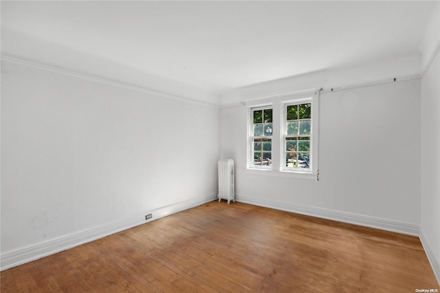 empty room featuring wood-type flooring, radiator heating unit, and crown molding