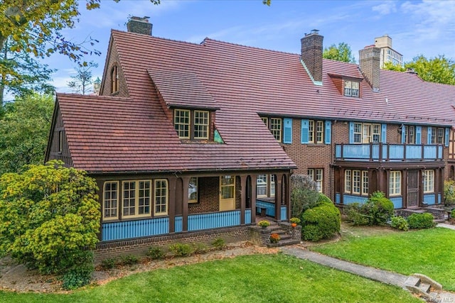 back of property featuring brick siding, a lawn, covered porch, and a chimney